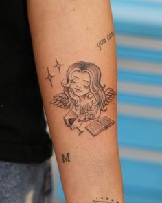 a woman's arm with a tattoo on it and an angel reading a book