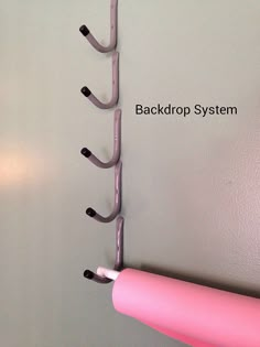 there is a pink wall hanging on the wall with black hooks and a white background