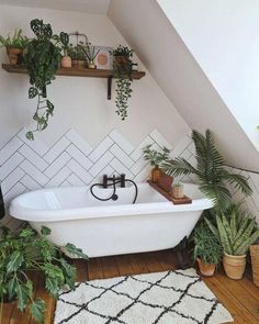 a white bath tub sitting under a slanted ceiling next to plants and potted plants