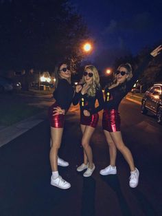 three beautiful young women standing next to each other on a street at night with their arms in the air