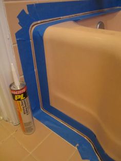 a bathtub with blue tape on it and a can of paint next to it