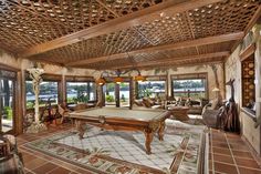 a pool table in the middle of a living room with lots of windows and furniture