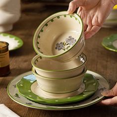 a stack of green and white dishes on top of each other with hands reaching for one