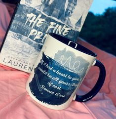 a coffee mug sitting on top of a bed next to a book cover and pillow