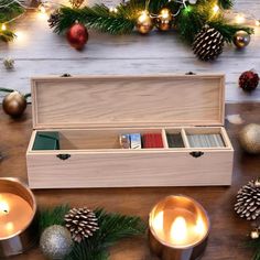 a wooden box filled with books next to candles and pine cones on top of a table