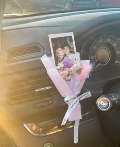 a bouquet of flowers is placed on the dashboard of a car with a photo attached to it