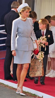 the woman is walking down the red carpet with her hand in her pocket and holding flowers