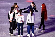 four people standing on an ice rink with one person holding the other's hand