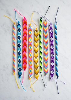 four colorful braided bracelets are lined up on a marble surface with string attached to them