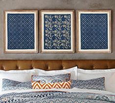 two framed pictures hang above a bed with blue and white comforter, pillows, and decorative artwork