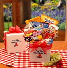 a gift box filled with candy sits on a checkered tablecloth next to grapes