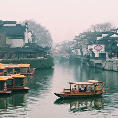 two boats are traveling down the river in front of some buildings on either side, with yellow umbrellas over them