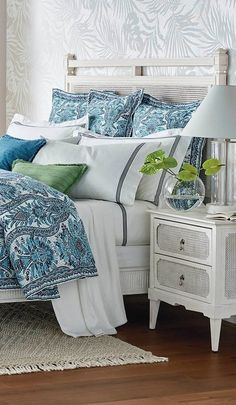 a white bed with blue and green pillows on top of it next to a night stand