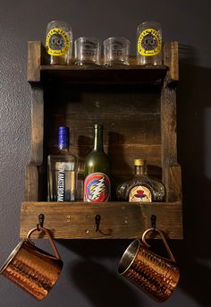 an old wooden shelf with two mugs and bottles on it, hanging from the wall