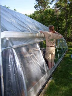 a man standing on the side of a green house with plastic covering it's walls