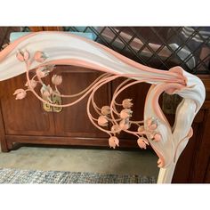 an ornate pink and white bed frame with flowers on the top, in front of a wooden dresser