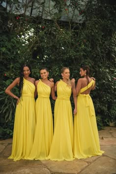 four beautiful women in yellow dresses posing for the camera with trees and greenery behind them