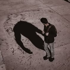 a man is standing on the sidewalk and looking at his cell phone, casting a shadow