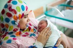 a woman holding a baby in her arms and wearing a headscarf on top of her head