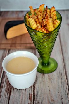 a green glass vase filled with food next to a cup of coffee on top of a wooden table