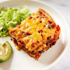 a white plate topped with lasagna, lettuce and an avocado