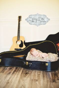 a baby is laying in a suit case next to an acoustic guitar on the floor