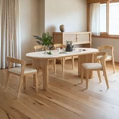 a table and chairs in a room with wood flooring, white walls and windows