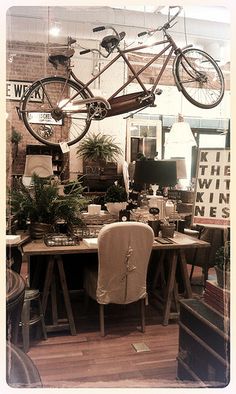 a bicycle hanging from the ceiling above a table with chairs and other items on it