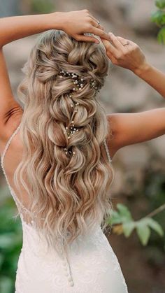 a woman with long blonde hair wearing a wedding dress and holding her hands on her head