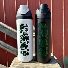 two black and white water bottles sitting next to each other on a wooden table in front of a red wall