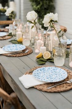 the table is set with plates, candles and lemons in mason jar vases