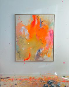 an abstract painting is being displayed in front of a white wall with paint splattered on the floor