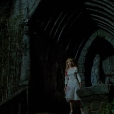 a woman in a white dress is walking through a tunnel with her hand on her hip