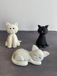 three ceramic cats sitting next to each other on a table with one black cat and one white cat