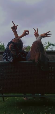 two people sitting on a bench with their hands in the air