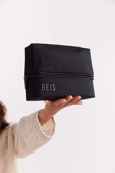 a woman holding up a black bag with the word beis on it