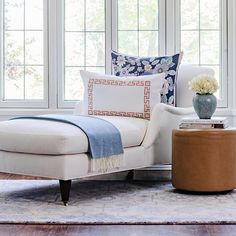 a white chair and ottoman in front of three windows with blue and white pillows on them