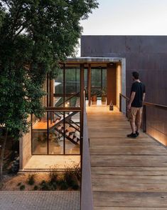 a man standing on a wooden walkway next to a building with glass walls and stairs