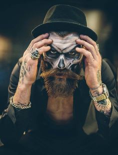 a man with his face painted like a skull wearing a top hat and holding his hands to his face