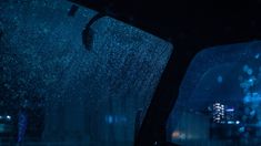 rain is falling down on the windshield of a car at night time with buildings in the background