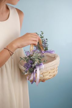 a woman in a white dress holding a basket with lavenders and greenery on it