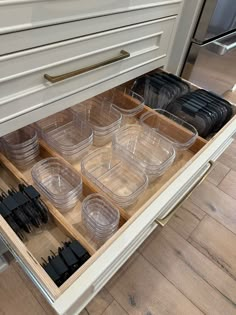 an open drawer in a kitchen filled with plastic containers and black lids on the drawers