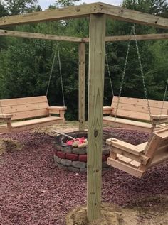 a wooden swing set with two swings and a fire pit in the middle of it