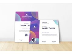 two certificates on top of each other in front of a white wall and wooden floor