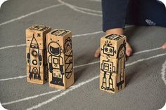 two wooden blocks with drawings on them are sitting on the floor next to a child's hand