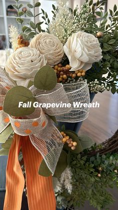 a vase filled with white flowers on top of a wooden table next to a wreath