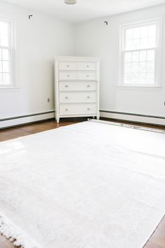 a white bed sitting in the middle of a room next to two windows and a dresser