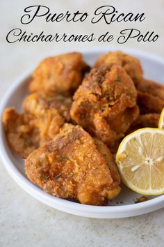 a white bowl filled with fried chicken next to lemon wedges and a slice of lime