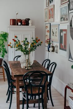 a dining room table with chairs and pictures on the wall above it, along with vases filled with flowers