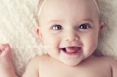 a smiling baby laying on top of a white blanket